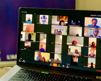 Open laptop shows screen of multiple faces in small boxes on screen like a large virtual meeting group